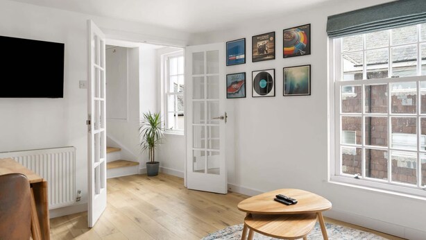 Un soggiorno moderno con una TV a schermo piatto, un tavolo rotondo in legno, una pianta in vaso e un'ampia finestra con vista sull'esterno.