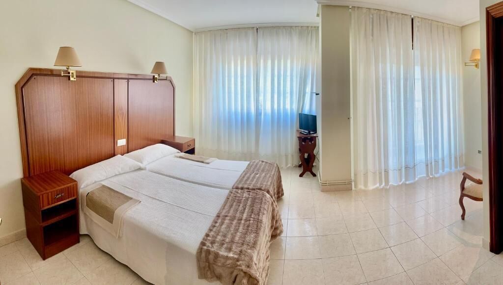 Een hotelkamer met een groot bed, twee nachtkastjes, een televisie en uitzicht op het buitenland door een raam met gordijnen.