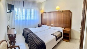 Hotellihuone, jossa on kaksi sänkyä, televisio, työpöytä ja lamppu.