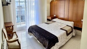 Hotellihuone, jossa on sänky, työpöytä, tuoli, yöpöytä ja ikkuna, jossa on verhot.