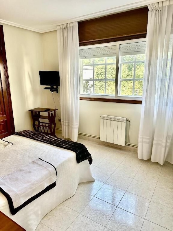 Une chambre à coucher avec un lit, une télévision, une fenêtre avec des rideaux et un radiateur.