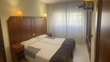Een hotelkamer met een groot bed, twee bedlampen, een houten hoofdbord, een nachtkastje en een raam met gordijnen.
