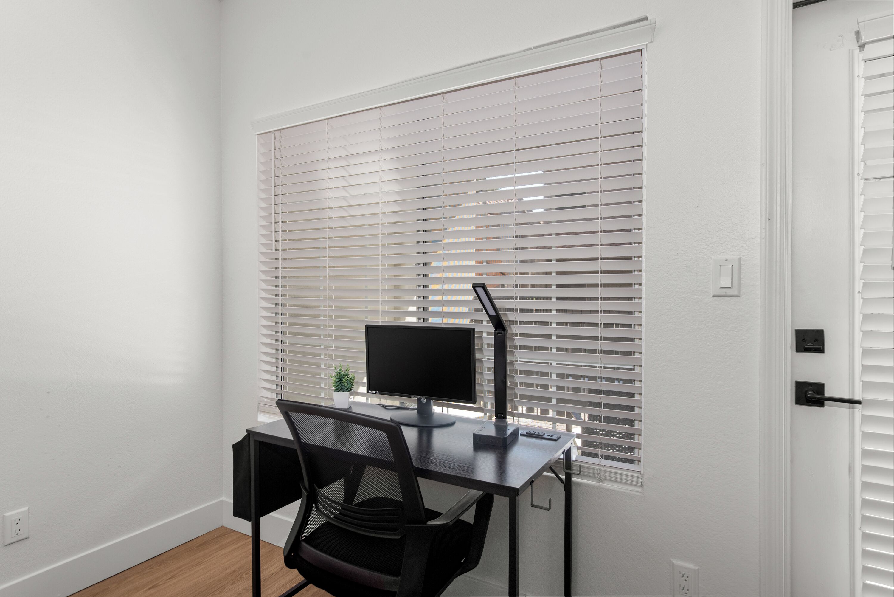 A room with a desk, computer, chair, and window blinds.