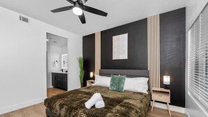 Un dormitorio moderno con cama, mesitas de noche, ventilador de techo y ventana con persianas.