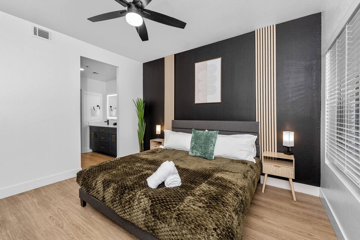 A modern bedroom with a bed, bedside tables, a ceiling fan, and a window with blinds.