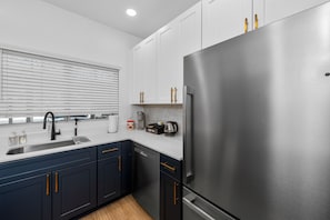 Una cocina moderna con refrigerador de acero inoxidable, un lavamanos con grifo y armarios blancos con tiradores dorados.