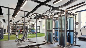 Un gimnasio con varios equipos de ejercicio, un área de césped artificial verde y un amplio ventanal que proporciona luz natural.