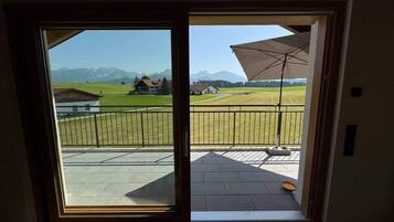 Ein Zimmer mit einer großen Schiebetür, die auf eine Terrasse im Freien mit Blick auf Berge und ein Wiesenfeld führt.