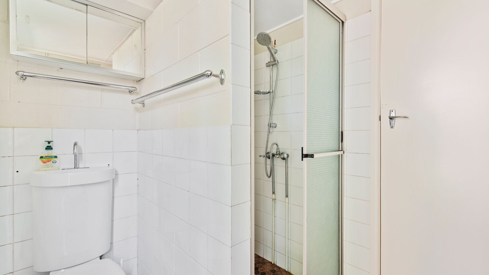 A bathroom with a toilet, sink, mirror, shower, and glass door.