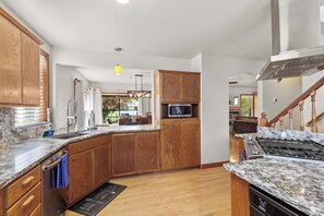 A modern kitchen with wooden cabinets, granite countertops, a built-in microwave, and a stainless steel range hood. - Lake City Hideaway (Coeur d'Alene)