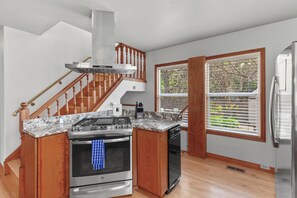 A kitchen with a central island, stainless steel appliances, wooden cabinetry, a stainless steel range hood, and a window with blinds. - Lake City Hideaway (Coeur d'Alene)