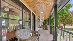 Varanda coberta com banco de vime, janelas amplas e vista para o exterior.