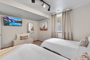 Un dormitorio con dos camas, un sofá, un televisor montado y una ventana con cortinas.