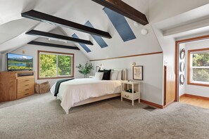 A bedroom with a bed, a dresser, a nightstand, a window with a view of greenery, and a skylight. - Lake City Hideaway (Coeur d'Alene)