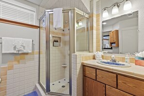 Un baño con ducha envuelta en vidrio, un lavamanos con azulejos decorativos azules y armarios de madera.