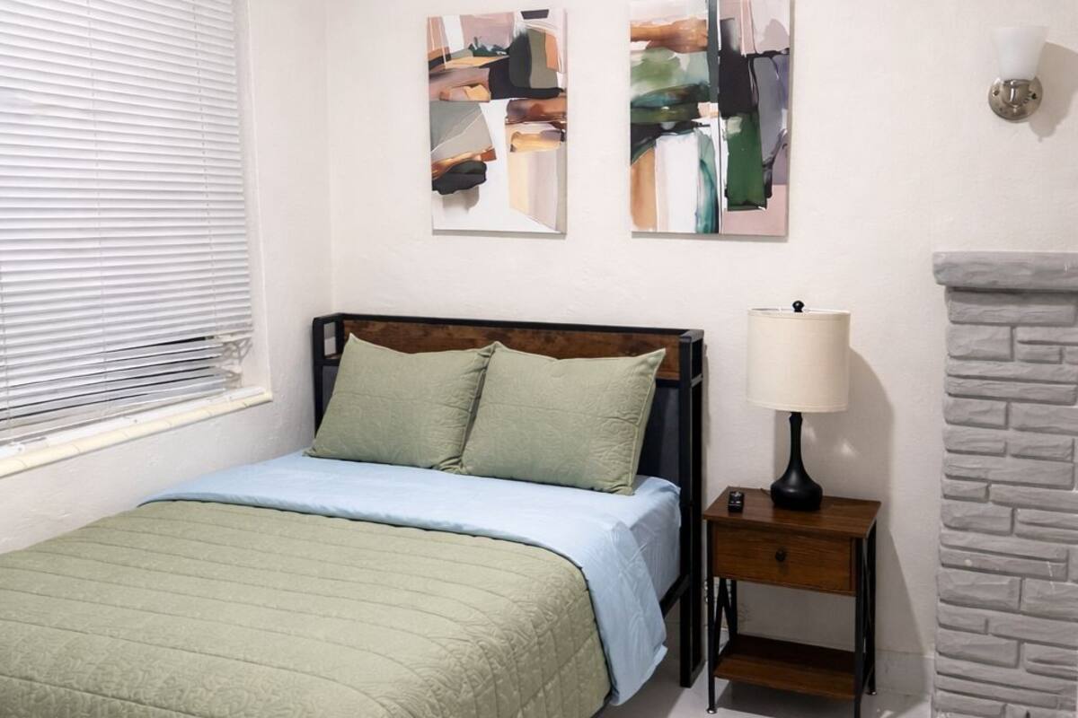 A bedroom with a bed, a nightstand, a lamp, a fireplace, and abstract wall art.