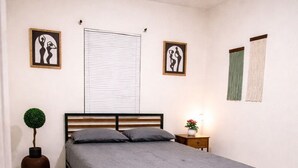 A bedroom with a bed, a nightstand, a potted plant, and artwork on the walls. - Riio Shores (Miami)