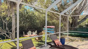 Un área de estar al aire libre techada con dos sillones de mimbre, cada uno con un cojín a rayas, y una maceta azul en el suelo.