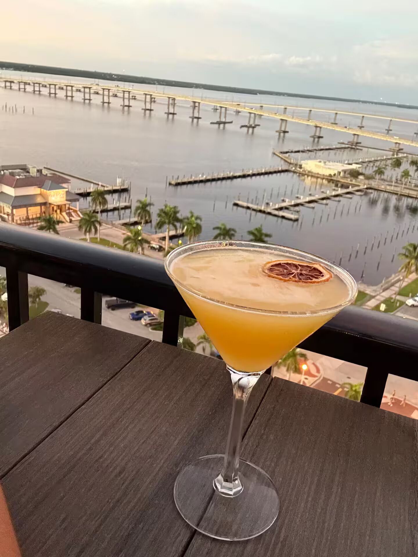 Een cocktail op een balkon met uitzicht op een jachthaven en een brug in de verte.