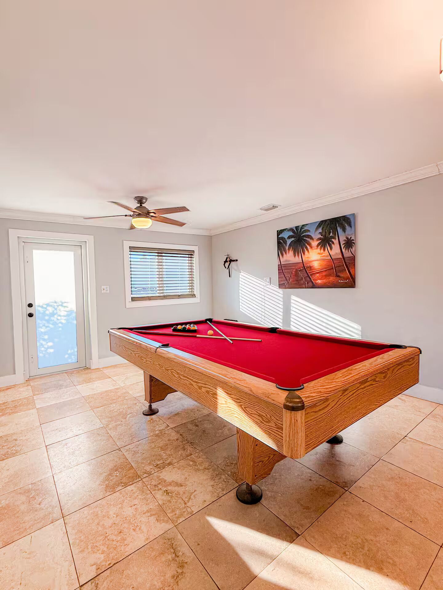 A pool table in a room with a ceiling fan, a door, and a window with blinds.