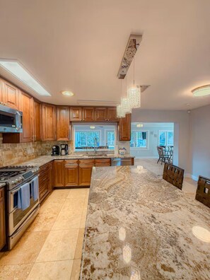 A modern kitchen with wooden cabinets, a large island, and a view to the dining area. - North Breeze, lake view with heated Pool (North Fort Myers)