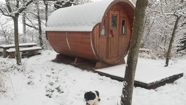 Uma cabana de madeira com telhado coberto de neve, uma porta de madeira e um banco por perto.