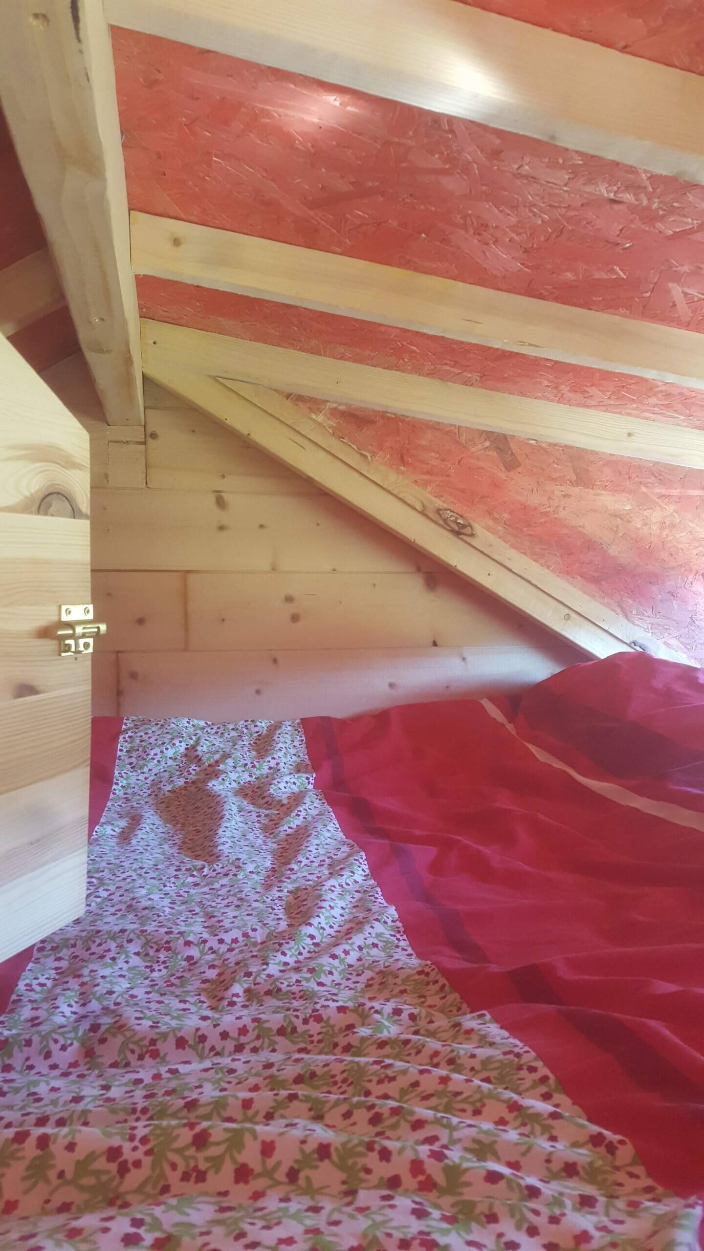 Een houten trap met een kleurenschema van rood en beige, een bed met een bloemenprint en een zichtbare deurklink.