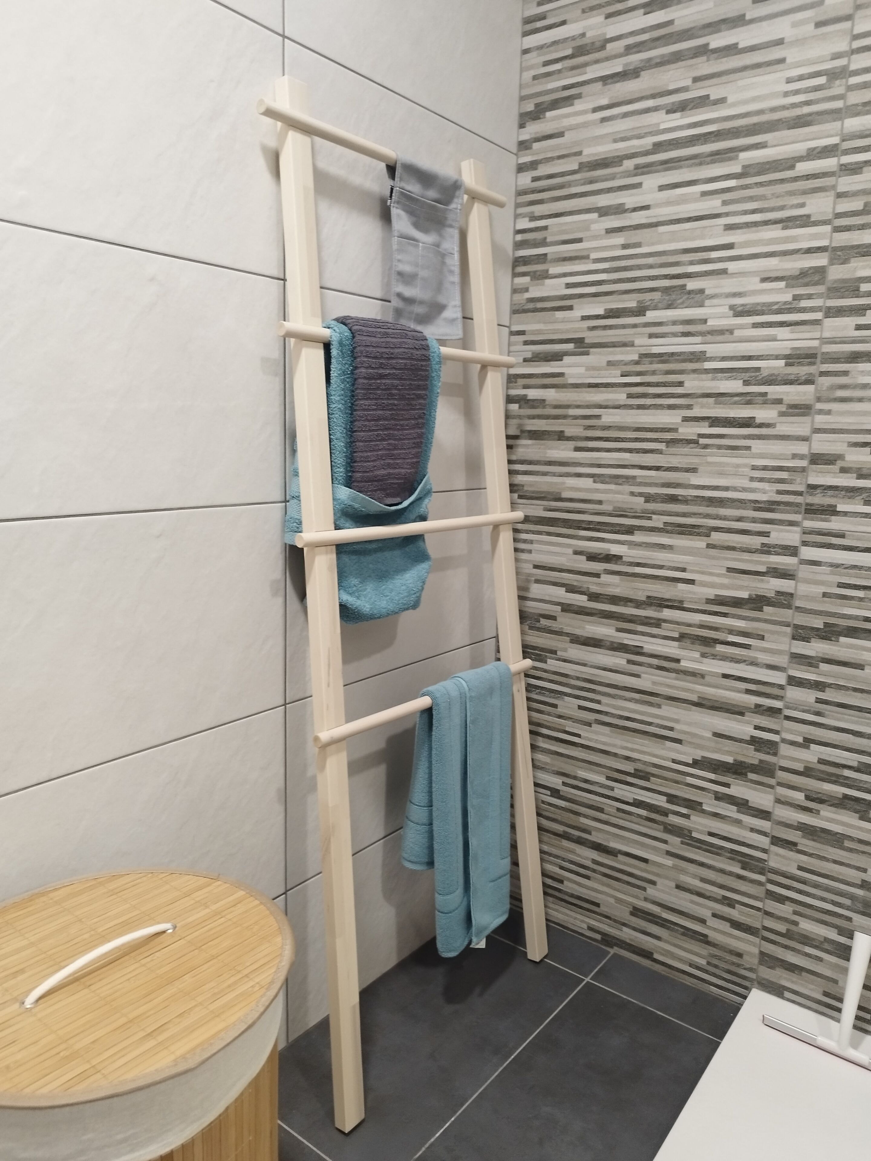 Une salle de bain avec un porte-serviettes en bois sur lequel sont posées deux serviettes, des toilettes et un lavabo surmonté d’un tapis en bambou.