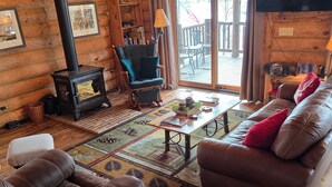 A log cabin interior with a fireplace, leather sofa, and a dining area.