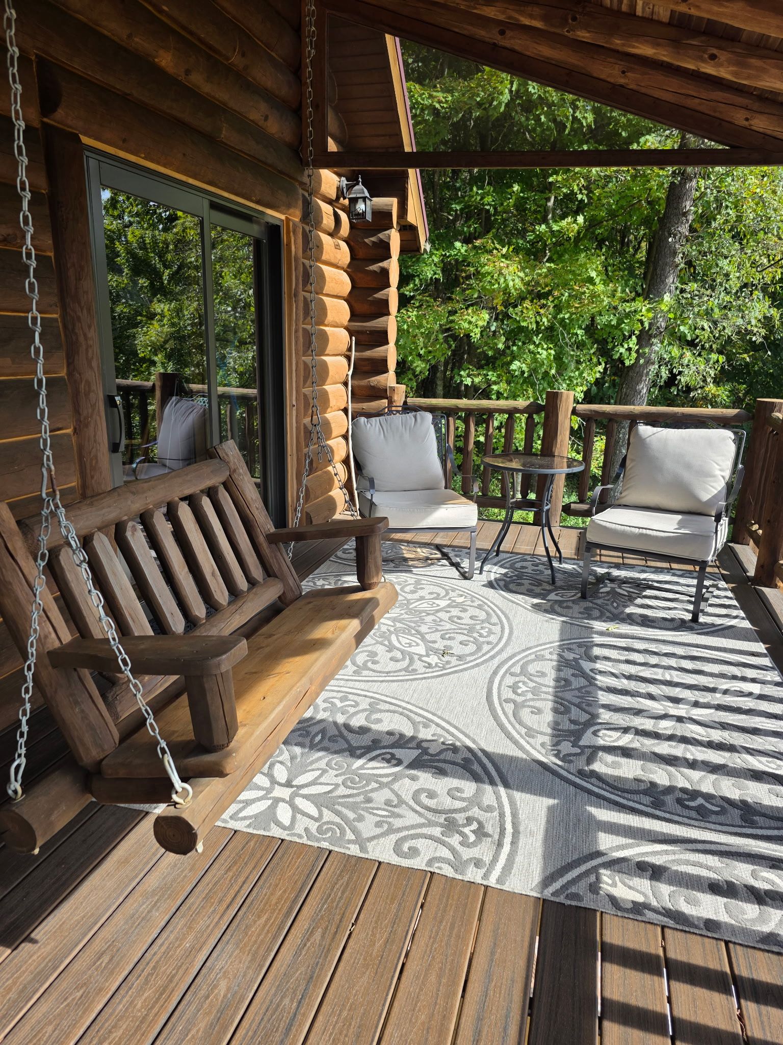 Una terraza de madera con una silla hamaca, un banco acolchado y dos sillas.