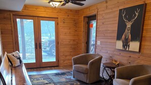 A wooden interior with a ceiling fan, a bench, two armchairs, a rug, and a deer painting.