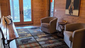 A wooden interior with a ceiling fan, a bench, two armchairs, a rug, and a deer painting.