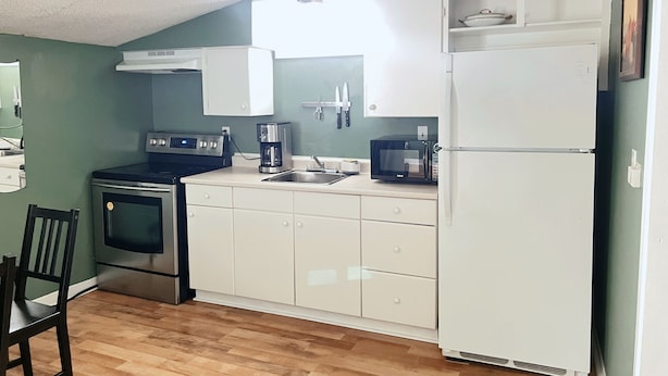 A compact kitchen with white cabinets, a microwave, a stove, and a refrigerator.