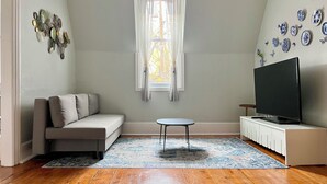 A living room with a sofa, a small table, a TV, and a window with curtains.