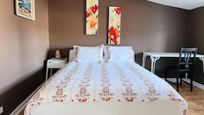 A bedroom with a bed, a desk, and two paintings on the wall.