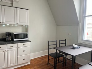 Una cocina con armarios blancos, microondas, cafetera y una mesa de comedor con sillas.