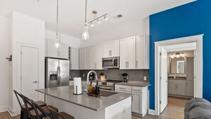 Uma cozinha moderna com armários brancos, eletrodomésticos de aço inoxidável e uma ilha central com banquetas.