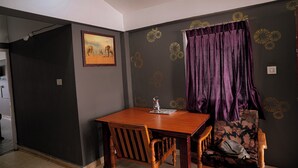 Ein Zimmer mit einem Holztisch, einem Stuhl, einer Couch, einem violetten Vorhang und einer Wand mit dekorativem Muster.
