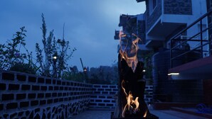 Ein Feuer brennt in einem Metallbehälter auf einer Terrasse mit einer Ziegelwand und einem Gebäude im Hintergrund.