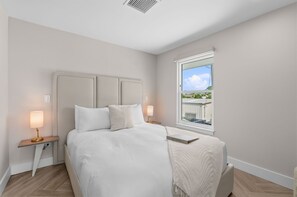 Een slaapkamer met een bed, nachtkastjes, een raam met uitzicht en een ventilatie rooster.