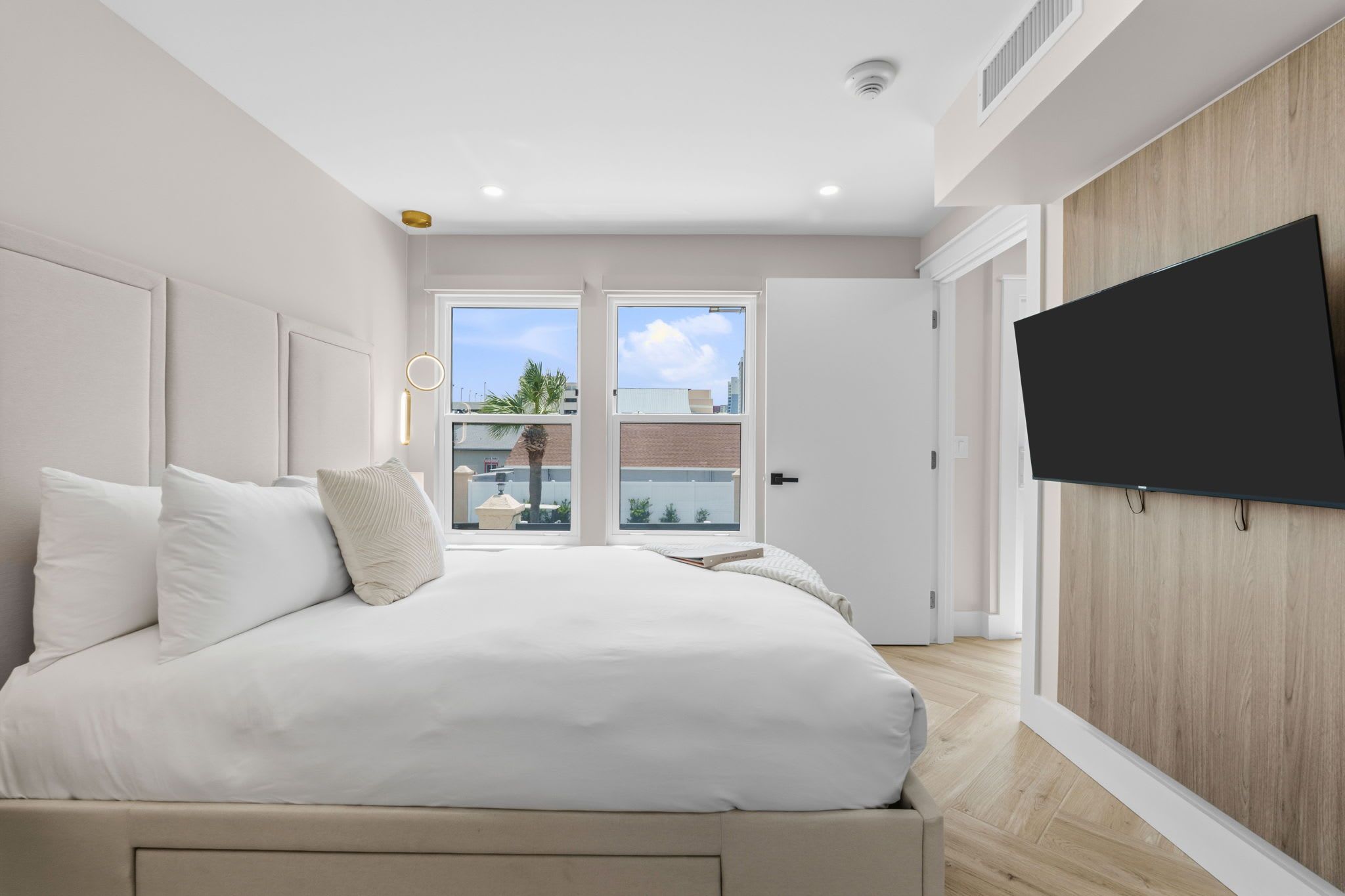 A bedroom with a bed, a TV mounted on the wall, and a view of the outside through the door.