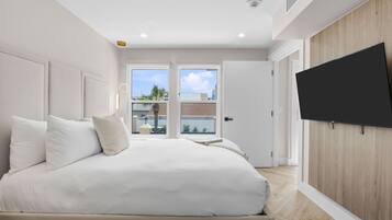 A bedroom with a bed, a TV mounted on the wall, and a view of the outside through the door.