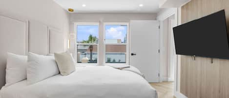 A bedroom with a bed, a TV mounted on the wall, and a view of the outside through the door.