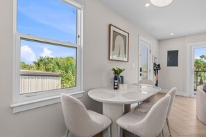 A modern dining area with a round table and four chairs, a framed artwork above the table, and a view of greenery outside. - Coastal  2 BR w/ Private Balcony & Lakeview (Panama City Beach)