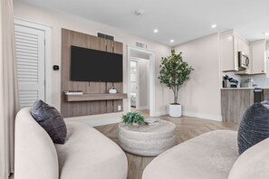 A modern living room with a flat-screen TV, a potted plant, and a round coffee table. - Coastal  2 BR w/ Private Balcony & Lakeview (Panama City Beach)
