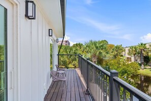 Una terraza de madera con barandilla, una mesa con sillas y vistas a un cuerpo de agua y vegetación.