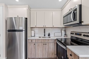 A modern kitchen with a stainless steel refrigerator, a microwave, a built-in oven, and a sink. - Modern Queen Studio | Steps to the Beach (Panama City Beach)