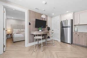 A modern kitchen with a built-in refrigerator, a dining area with stools, and a bedroom with a bed and nightstand. - Modern Queen Studio | Steps to the Beach (Panama City Beach)