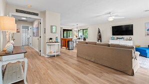 A spacious living area with a large sofa, a television, and a dining area with a table and chairs. - Salty Clover𓇼Vintage Vibes + Modern Comfort (Oak Island)