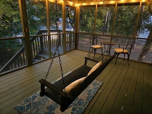 A covered porch with a swing, chairs, and a view of trees. - Salty Clover𓇼Vintage Vibes + Modern Comfort (Oak Island)
